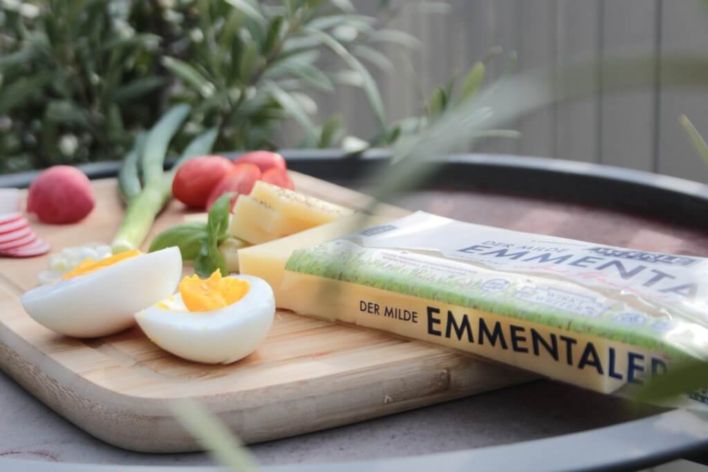 WOERLE Emmentaler liegt auf einem Holzbrett und ist garniert mit Tomaten und Ei.