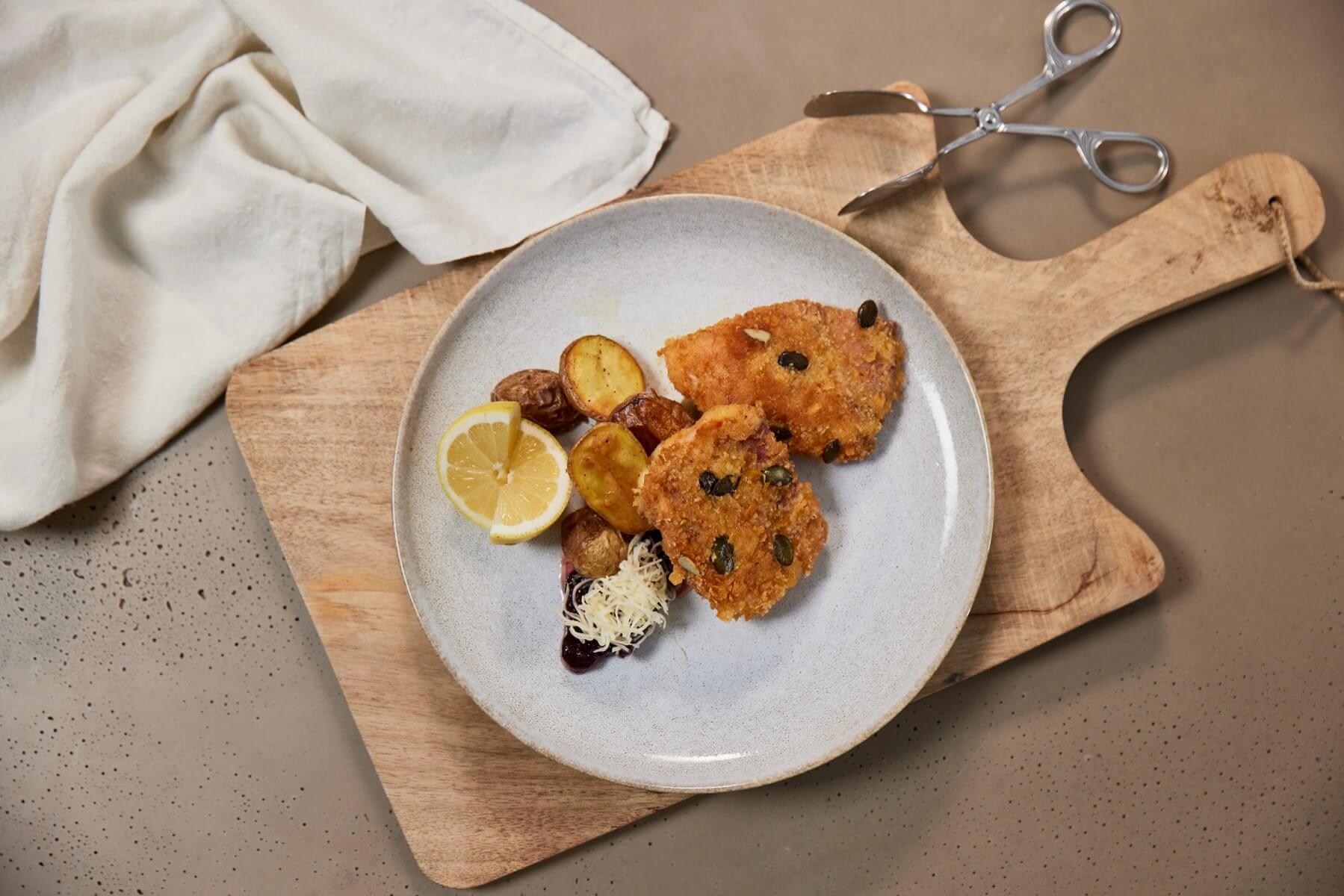 Kürbis Cordon bleu mit Kartoffeln auf einem weißen Teller, darunter ein Holzschneidebrett