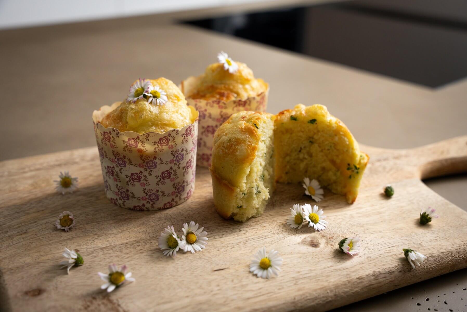 drei Stück Muffins mit Gänseblümchen auf einem Holz-Schneidebrett