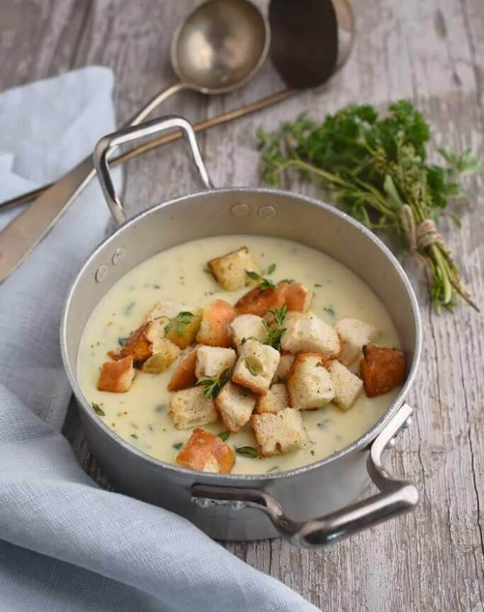 Käsesuppe in einem Topf mit Brot-Croutons oben drauf auf einem Holztisch