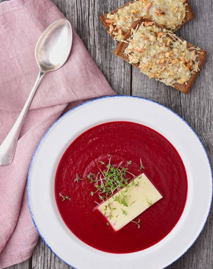 Rote Beete Suppe einer Suppenschüssel mit einem Stück Käse on Top und Brot nebenbei