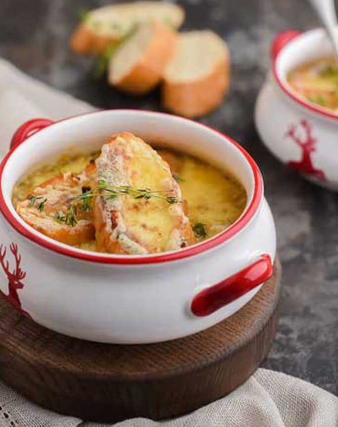 Zwiebelsuppe in einem weiß-roten Gefäß mit Brot oben drauf und auf der Seite